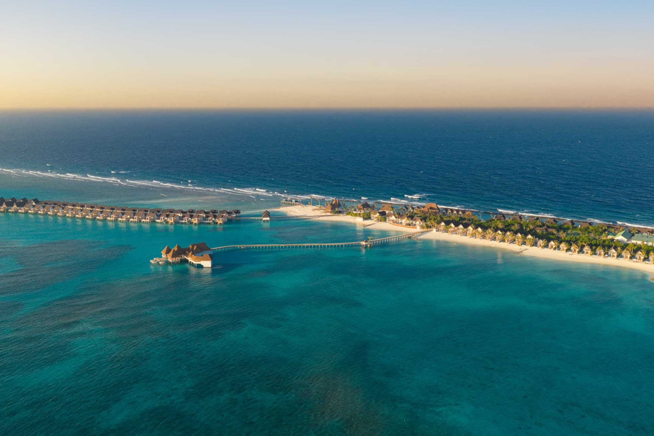 Aerial view of Meyyafushi Maldives at dusk, overwater villas lining the reef